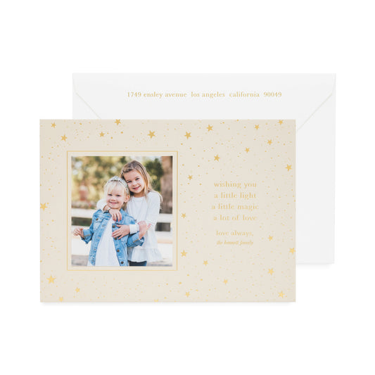 Custom holiday photo card with photo of two girls on a oat tan colored paper with champagne foil star pattern and 'wishing you a little light a little magic a lot of love"