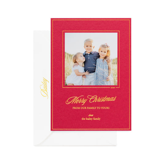 A red Christmas photo card with gold border and a photo of three kids and gold script text reading 'Merry Christmas' and 'From our family to yours' paired with a white envelope