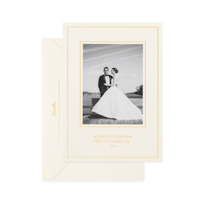 An elegant cream-colored wedding Christmas greeting card with a gold border and champagne gold script text printed with 'married christmas love the bennetts' with a cream envelope
