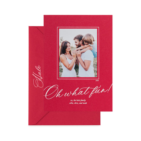 A holiday photo card on red paper featuring a photo of a family, white foil text reading 'Oh what fun!', and a red evenlope