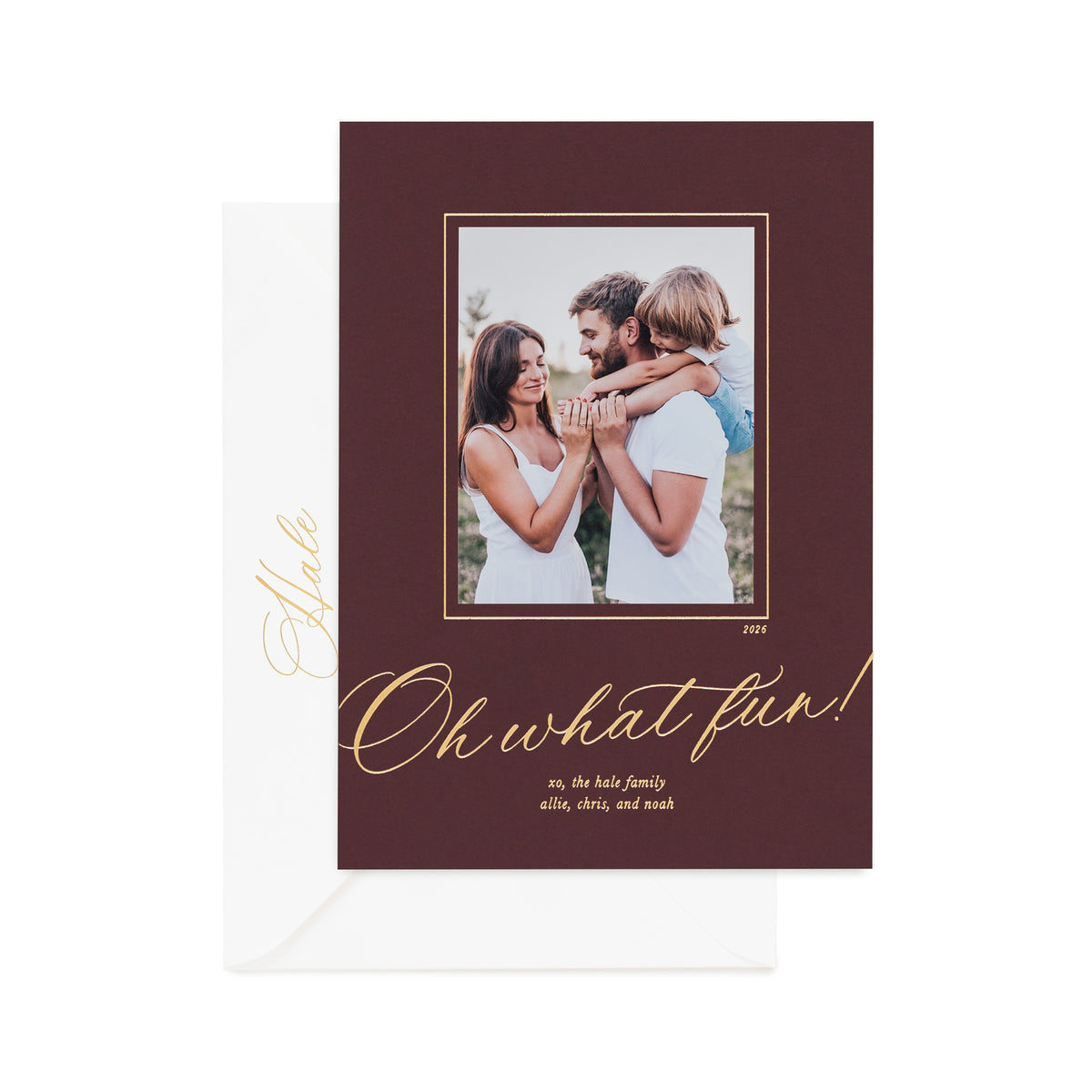 A holiday photo card on mulberry paper featuring a photo of a family, gold foil text reading 'Oh what fun!', and a white envelope behind it on a white background.