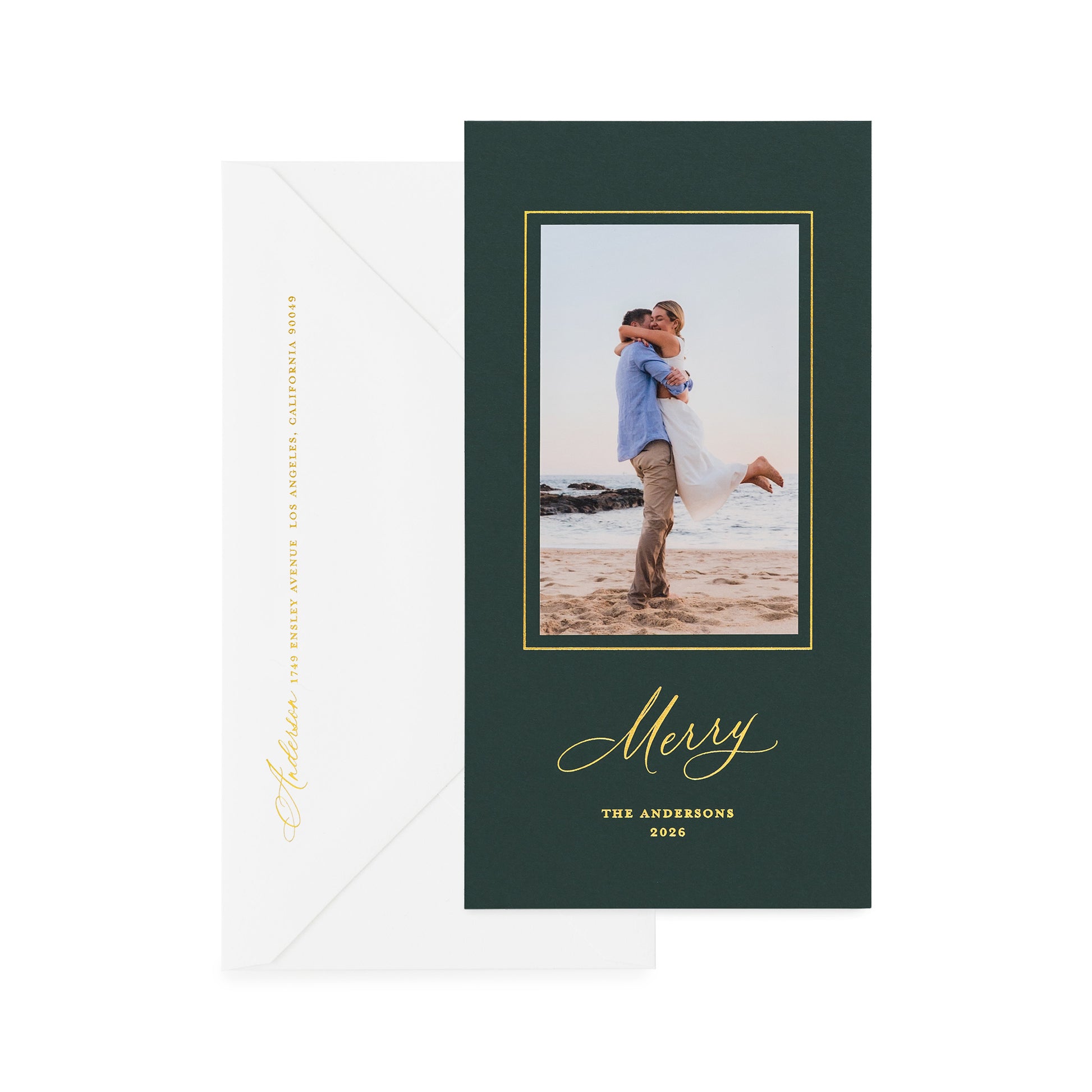 A vertical holiday card on racing green paper with gold foil details, shown with a white envelope behind it.