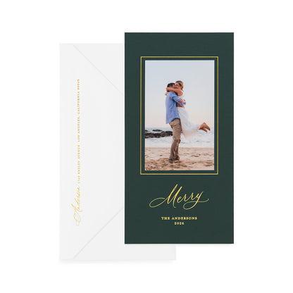 A vertical holiday card on racing green paper with gold foil details, shown with a white envelope behind it.