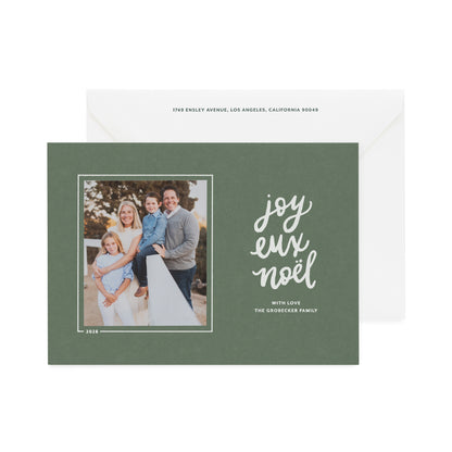 A dark sage green holiday photo card with a white envelope behind it, featuring a family photo on the left and the words 'joyeux Noel' in white script