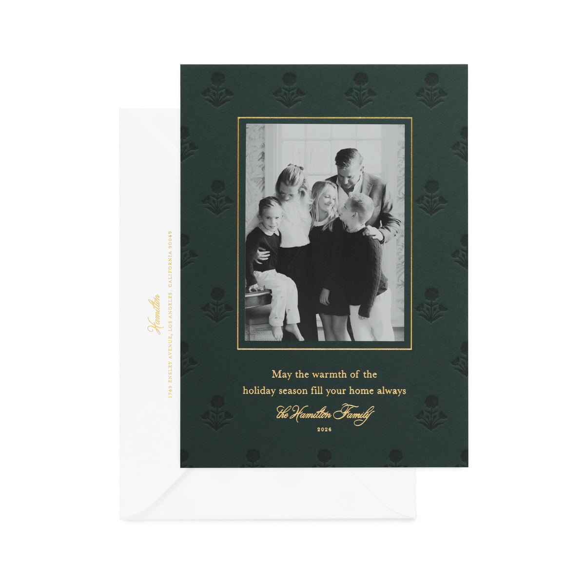 A dark green family holiday greeting card with a black-and-white family photo, gold border, and gold text, printed with 'may the warmth of the holiday season fill your home always,' shown with a white envelope
