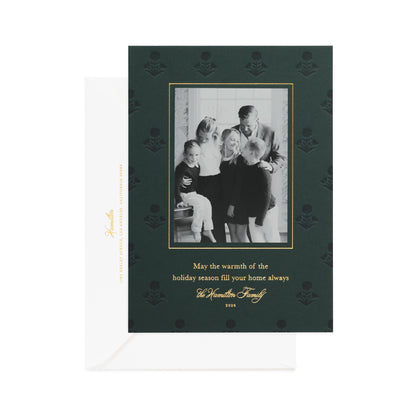 A dark green family holiday greeting card with a black-and-white family photo, gold border, and gold text, printed with 'may the warmth of the holiday season fill your home always,' shown with a white envelope