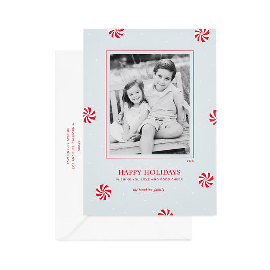 A personalized Christmas photo card on light blue paper with red and white peppermint candy icon pattern, a black-and-white family photo, printed with "merry christmas wishing you love and good cheer" with a white envelope and the address printed in red ink