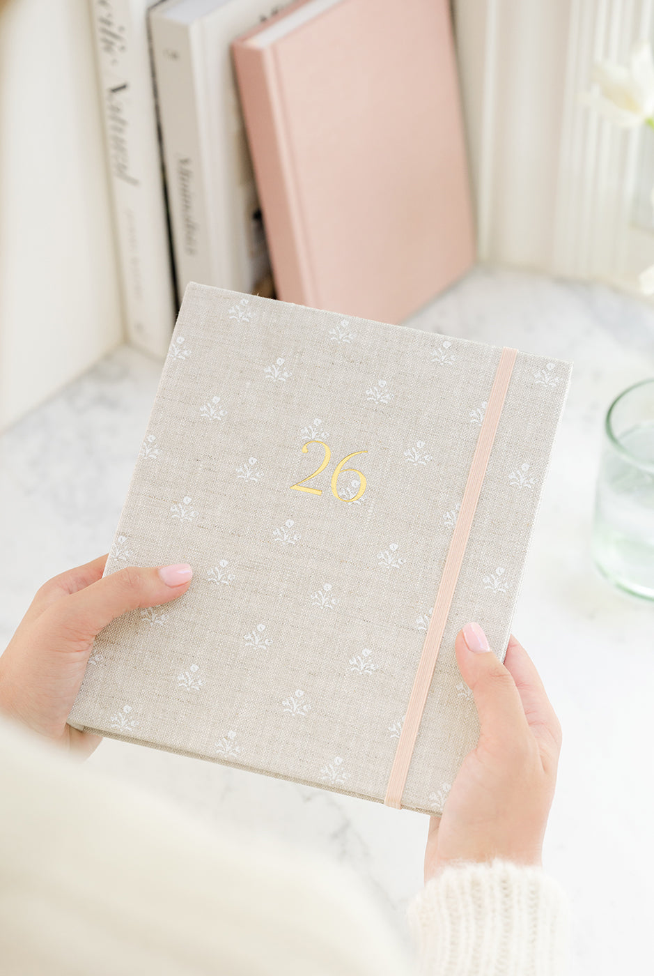 Person holding a flax floral agenda with '26 on cover in gold foil