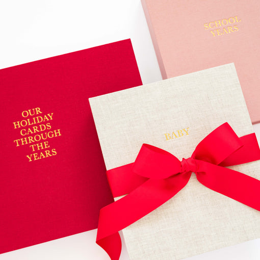 Red, flax, and pink keepsake books with text and ribbons on a white background