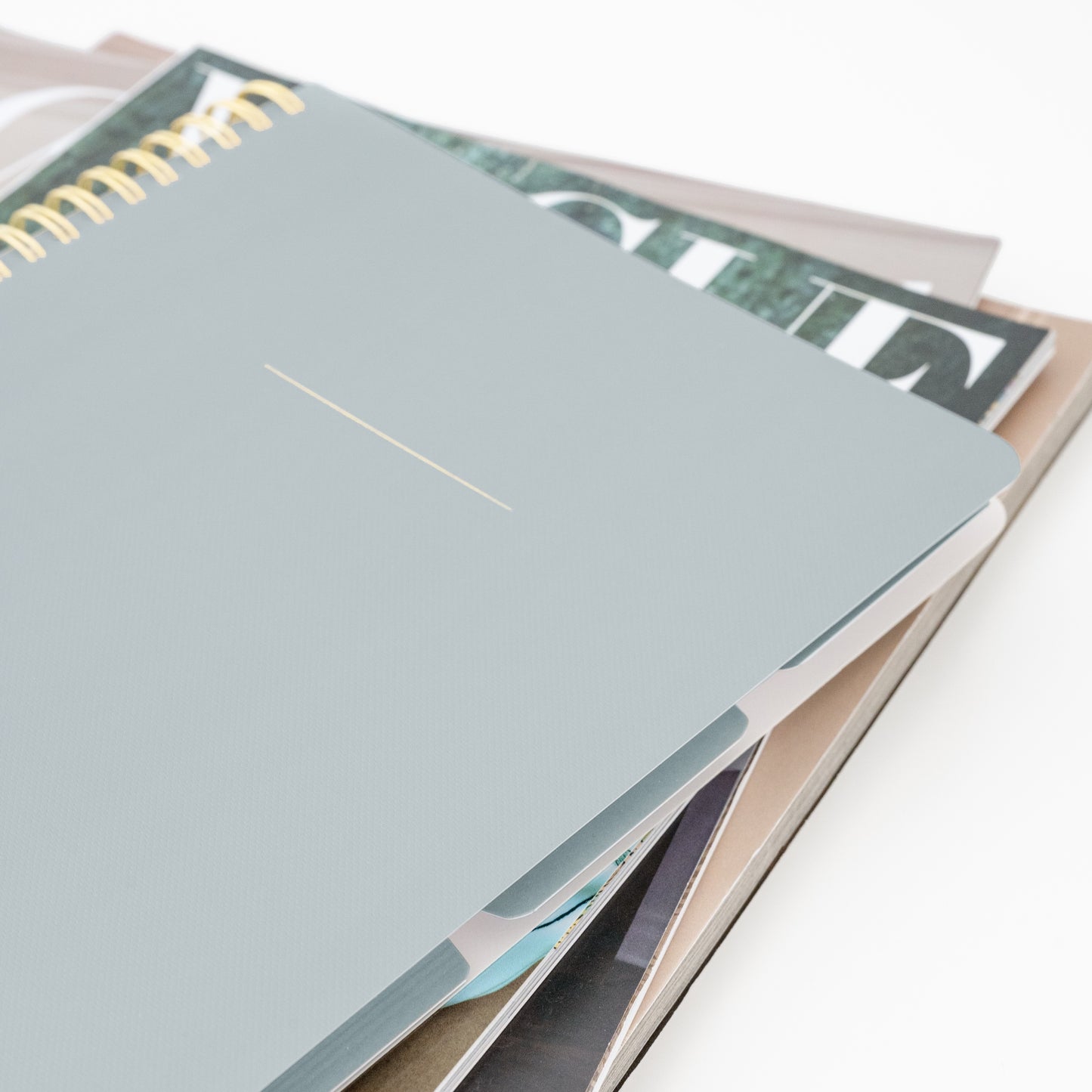 Dusty blue tabbed gold spiral notebook on stack of magazines