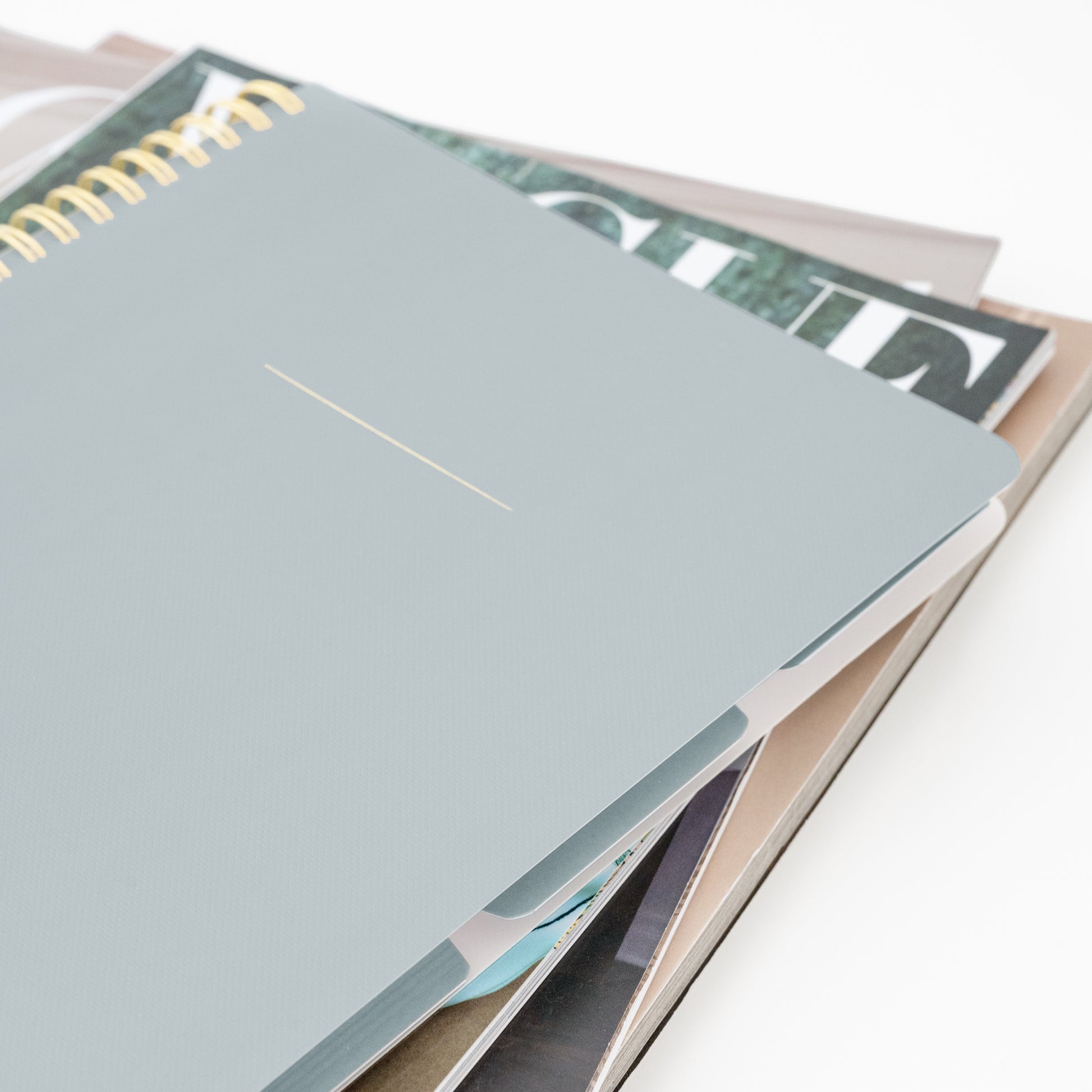 Dusty blue tabbed gold spiral notebook on stack of magazines