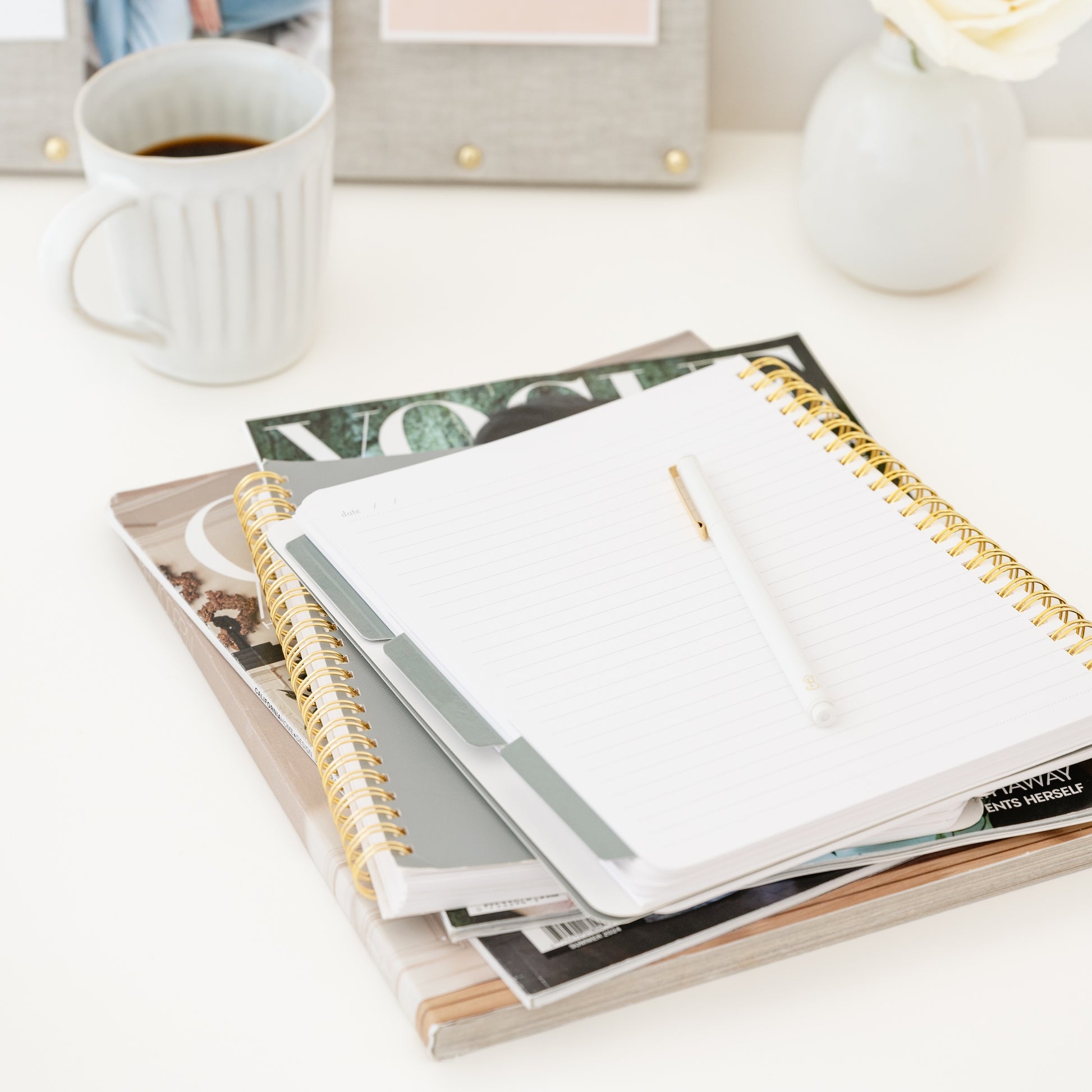 Open spiral notebook with blue tabs on a table with a cup of coffee and magazines in the background