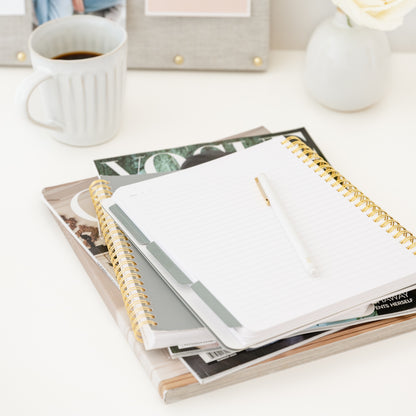 Open spiral notebook with blue tabs on a table with a cup of coffee and magazines in the background