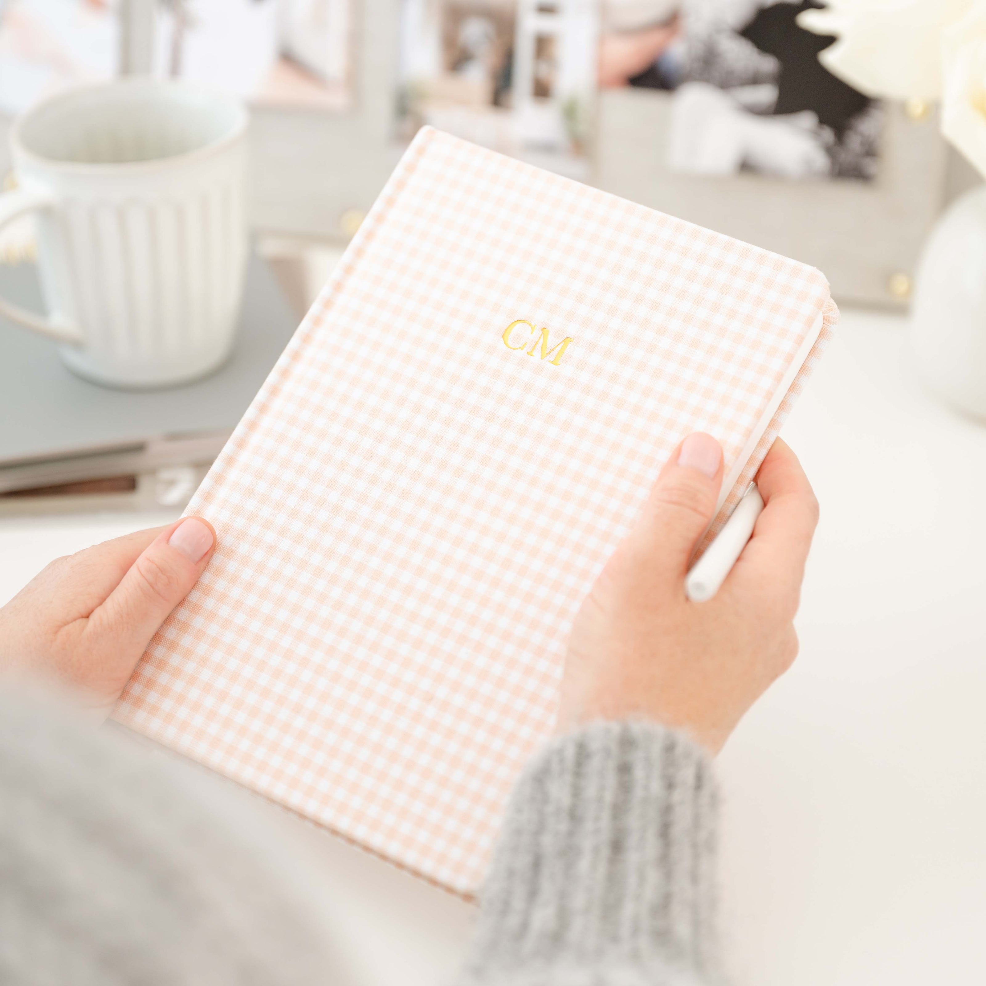 Hand holding a checkered notebook with 'CV' initials on a blurred indoor background