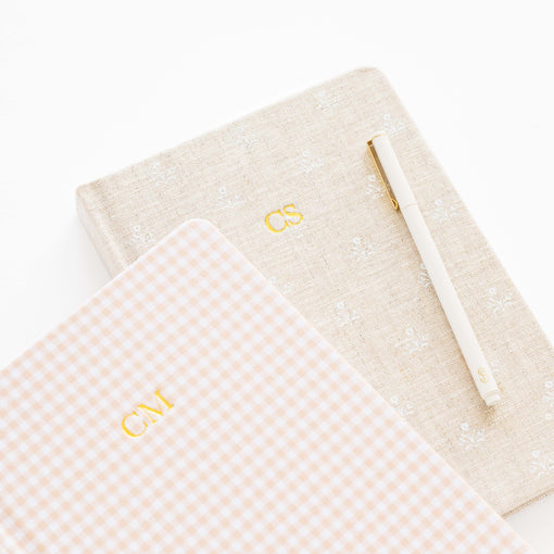 Two notebooks with monogrammed initials and a pen on a white background