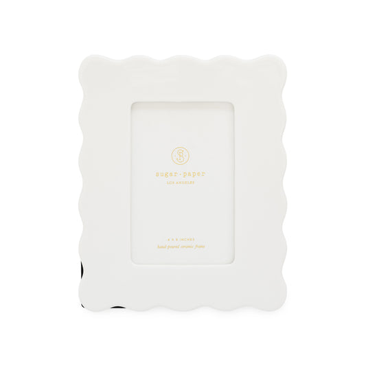 A white wavy scallop ceramic picture frame with a white cardstock in the center printed with 'sugar paper los angeles' and the specfications of the frame