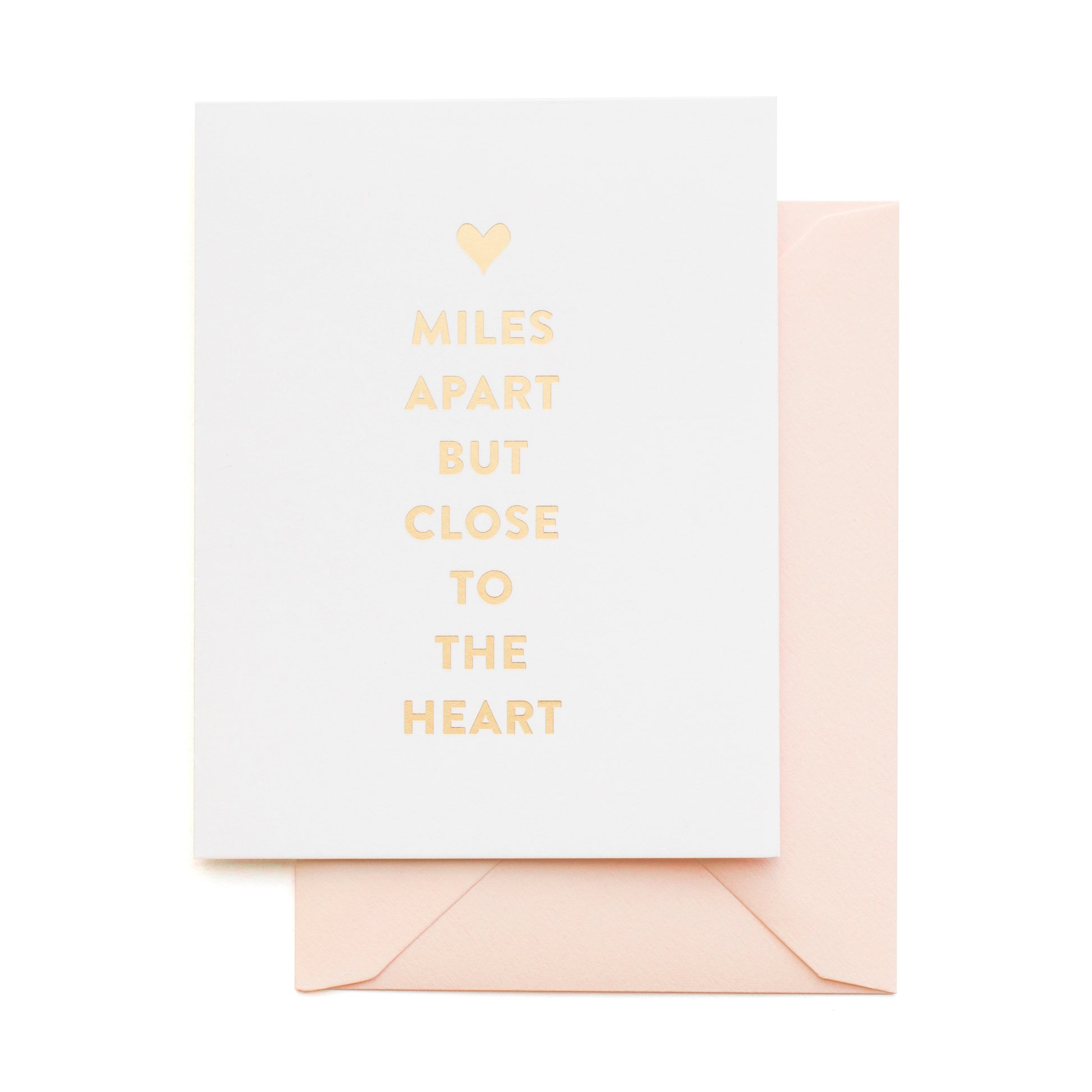 Greeting card with 'Miles apart but close to the heart' text with gold foil on a white background with a pink envelope.