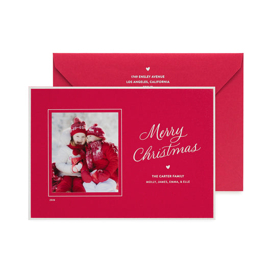A personalized Christmas photo card and matching envelope set in a vibrant red color. The front of the card features a photo of a family in winter clothing, alongside elegant white script reading 'Merry Christmas' and the family name with a white hand painted border around the card.