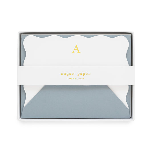 White bordered scallop with gold foil initial 'a' paired with a slate blue envelope in a white box with a white belly band with a 'sugar paper los angeles' gold foil logo