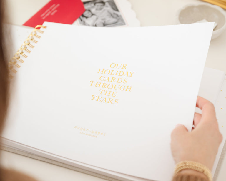 Holiday card book open to cover page printed with our holiday cards through the years in gold foil