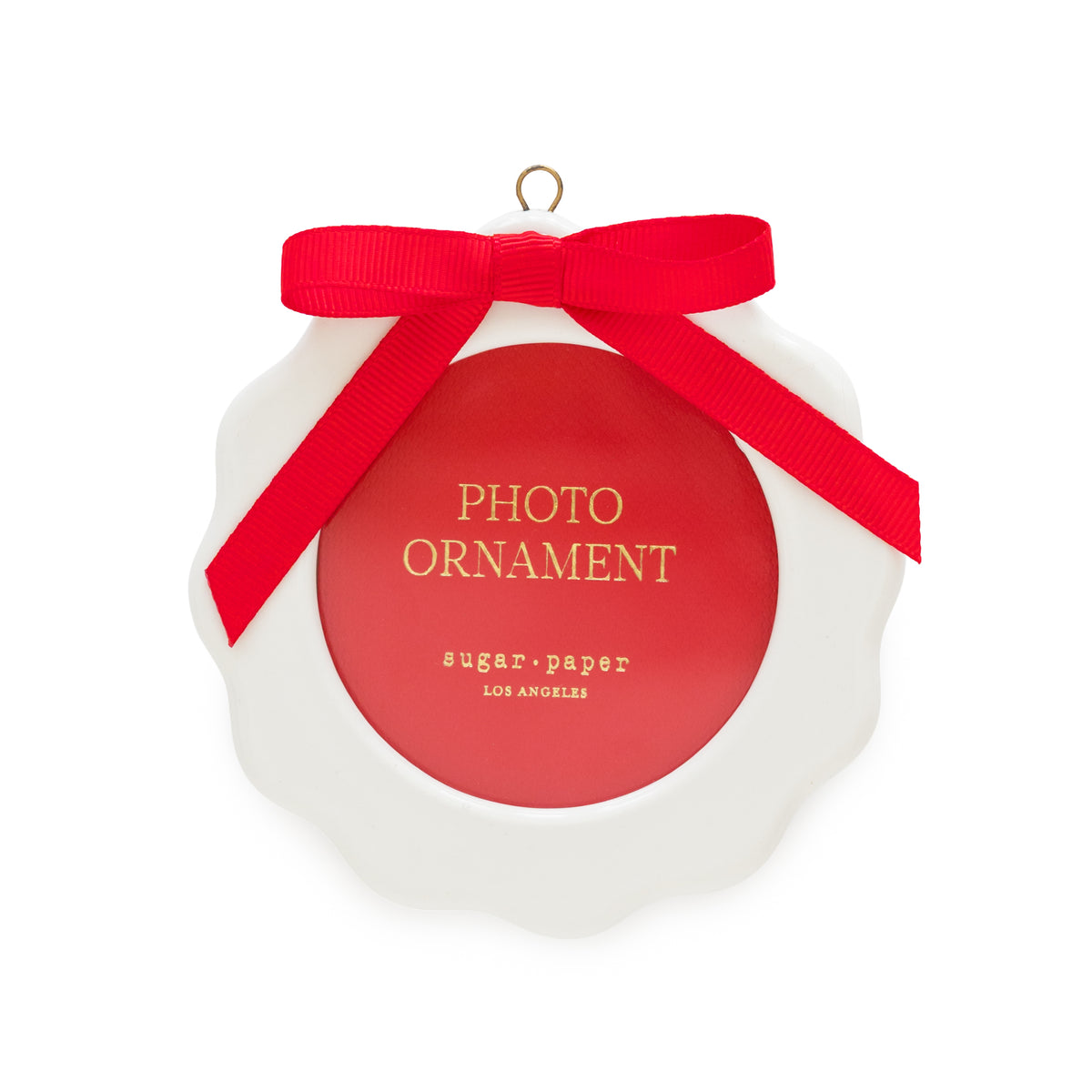 A white scalloped Christmas ornament with a red circular photo opening center, a red ribbon bow, and gold lettering that reads 'PHOTO ORNAMENT' and 'sugar paper LOS ANGELES'.