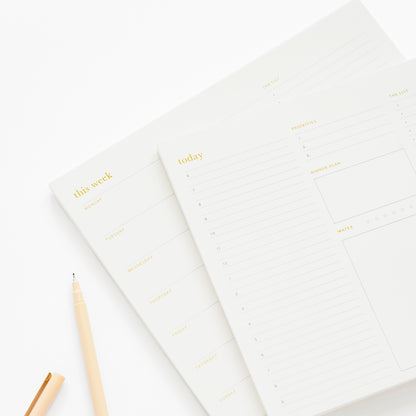 Stacked white and gold foil notepads with weekly and today prompts