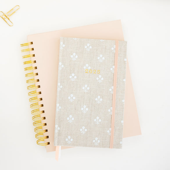 2025 Small Bound Flax Floral Agenda stacked on pink spiral planner