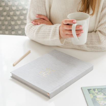 Person holding a white mug with a 2026 grey stripe fabric planner on the table in front of her