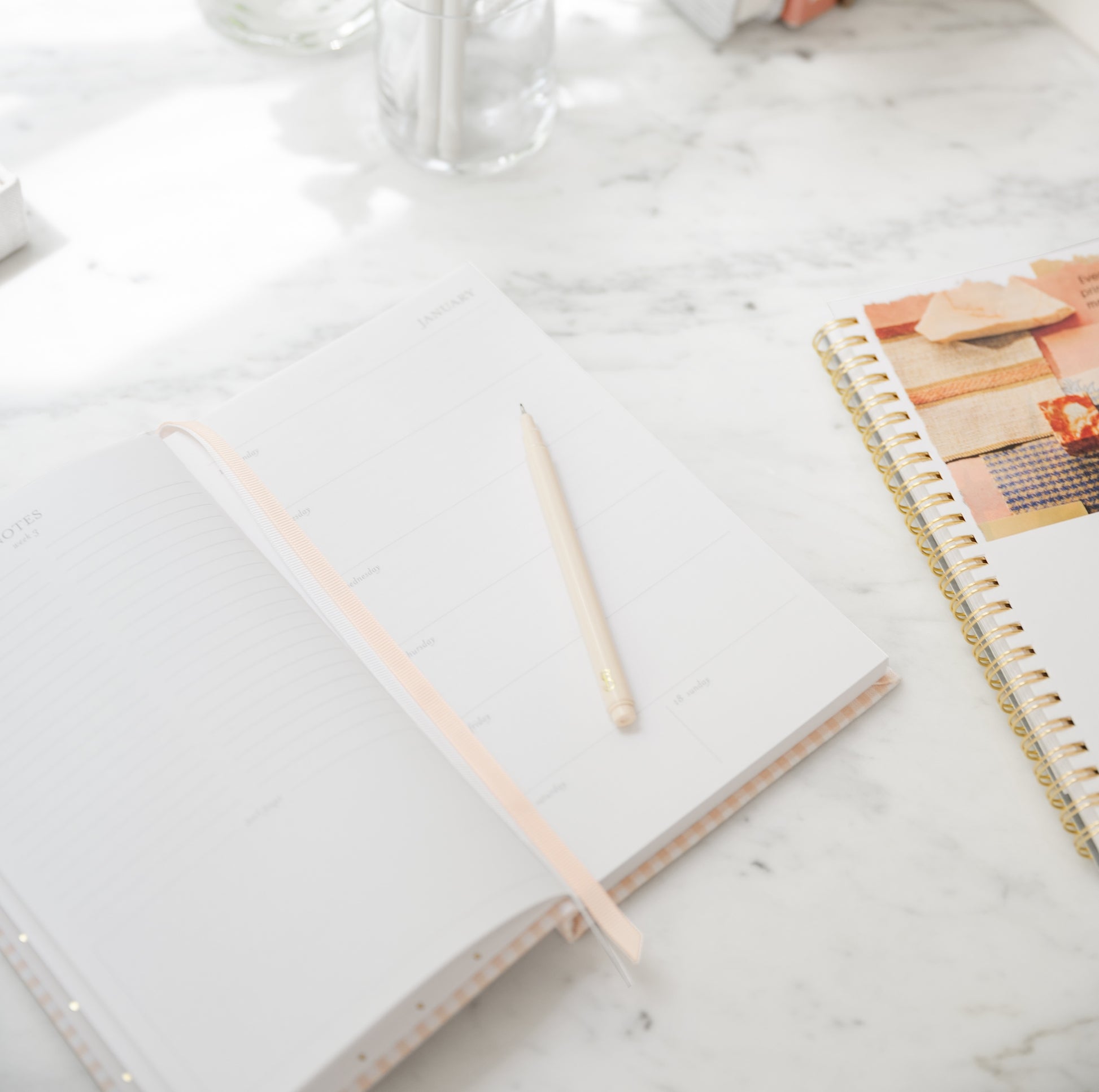 Open small pink gingham fabric agenda on kitchen table with notebook and pen