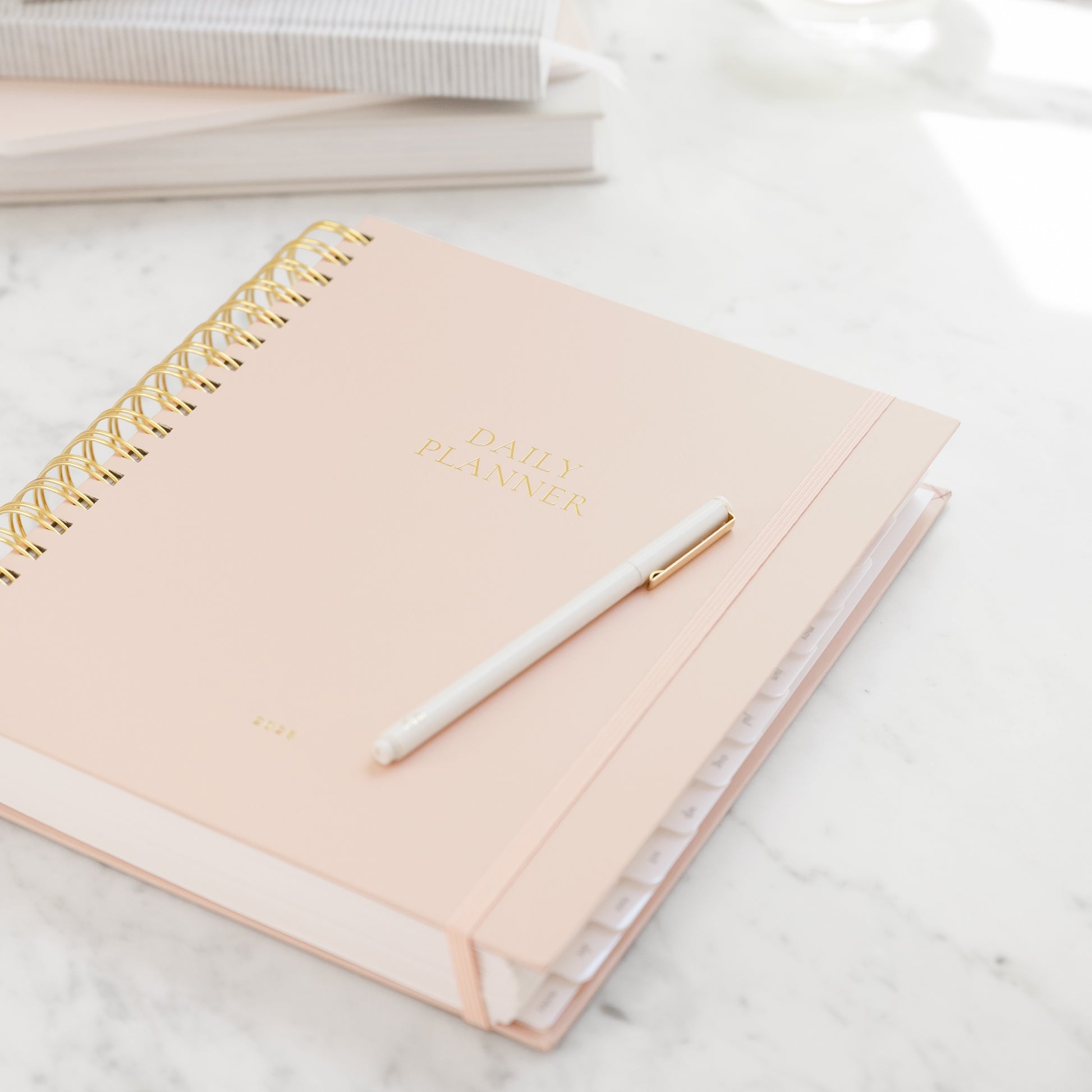 Blush Pink spiral planner with gold spiral binding and a white pen on a marble surface