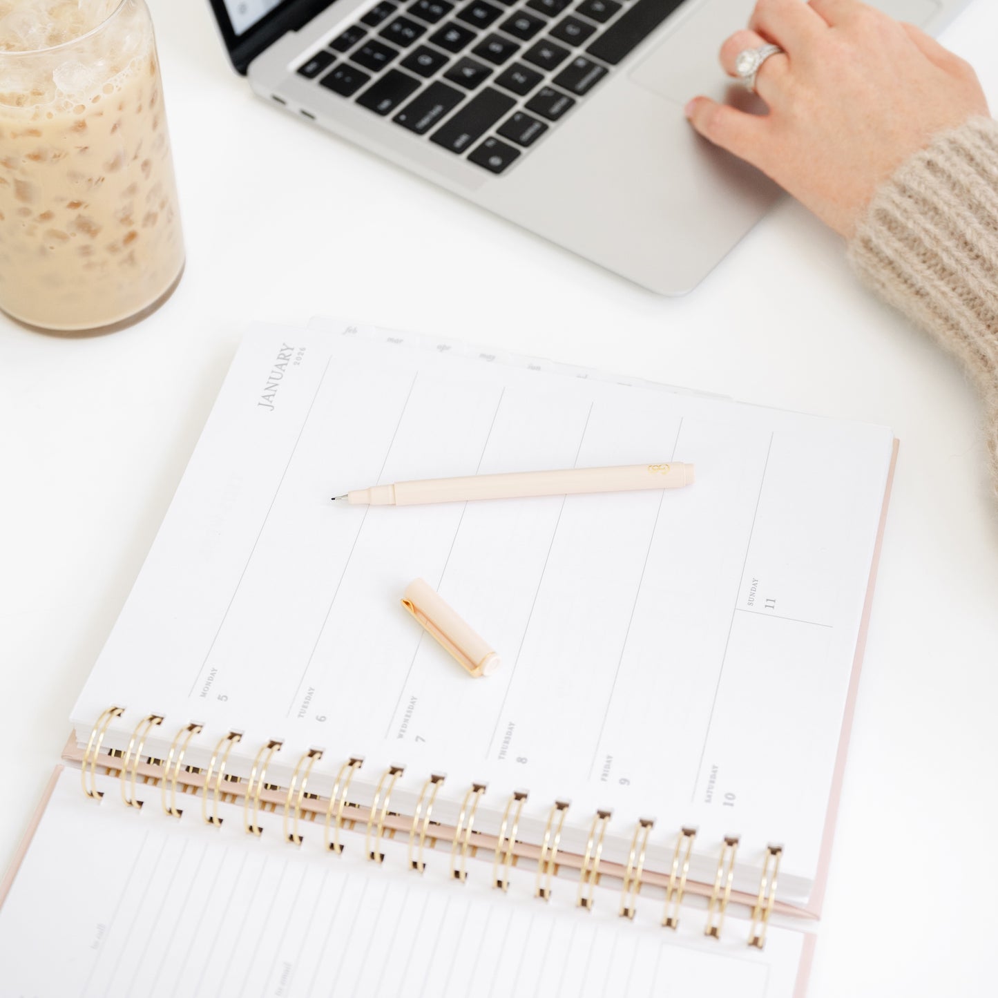Person using a laptop with an open pink spiral planner and pen