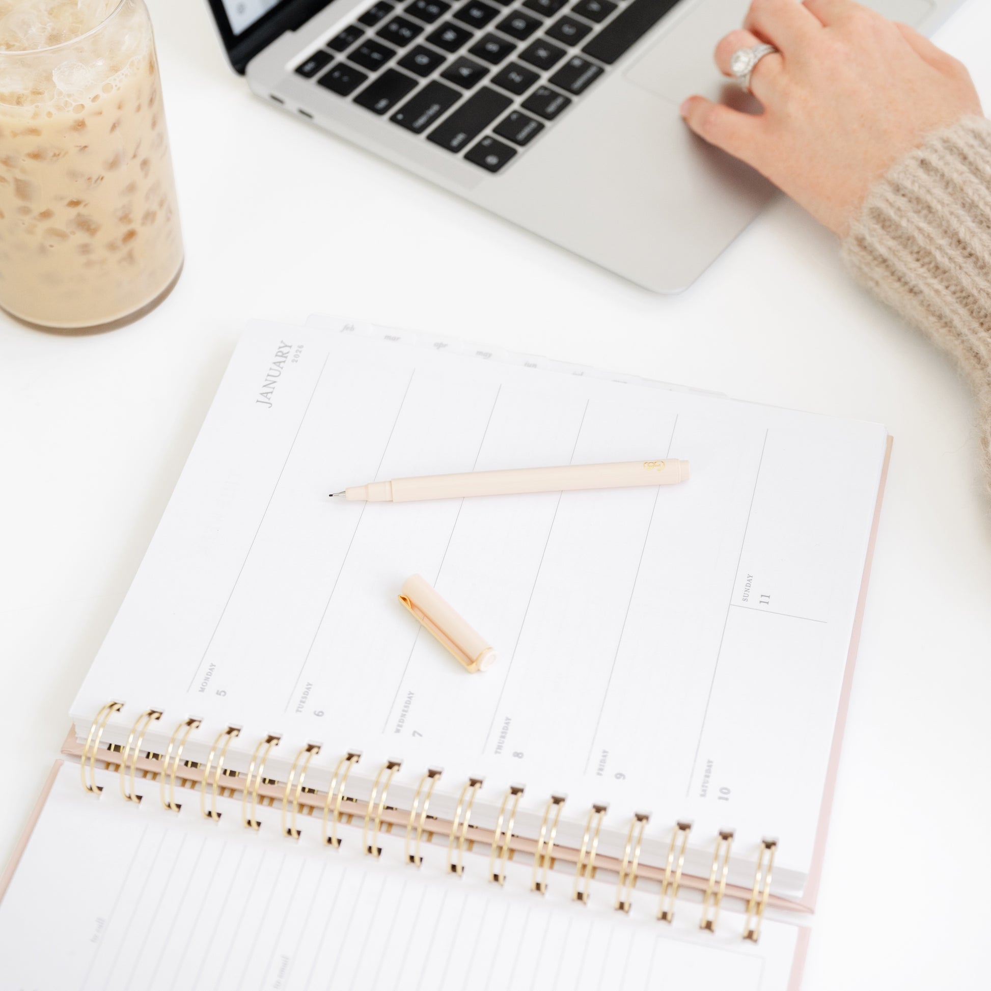 Person using a laptop with an open pink spiral planner and pen
