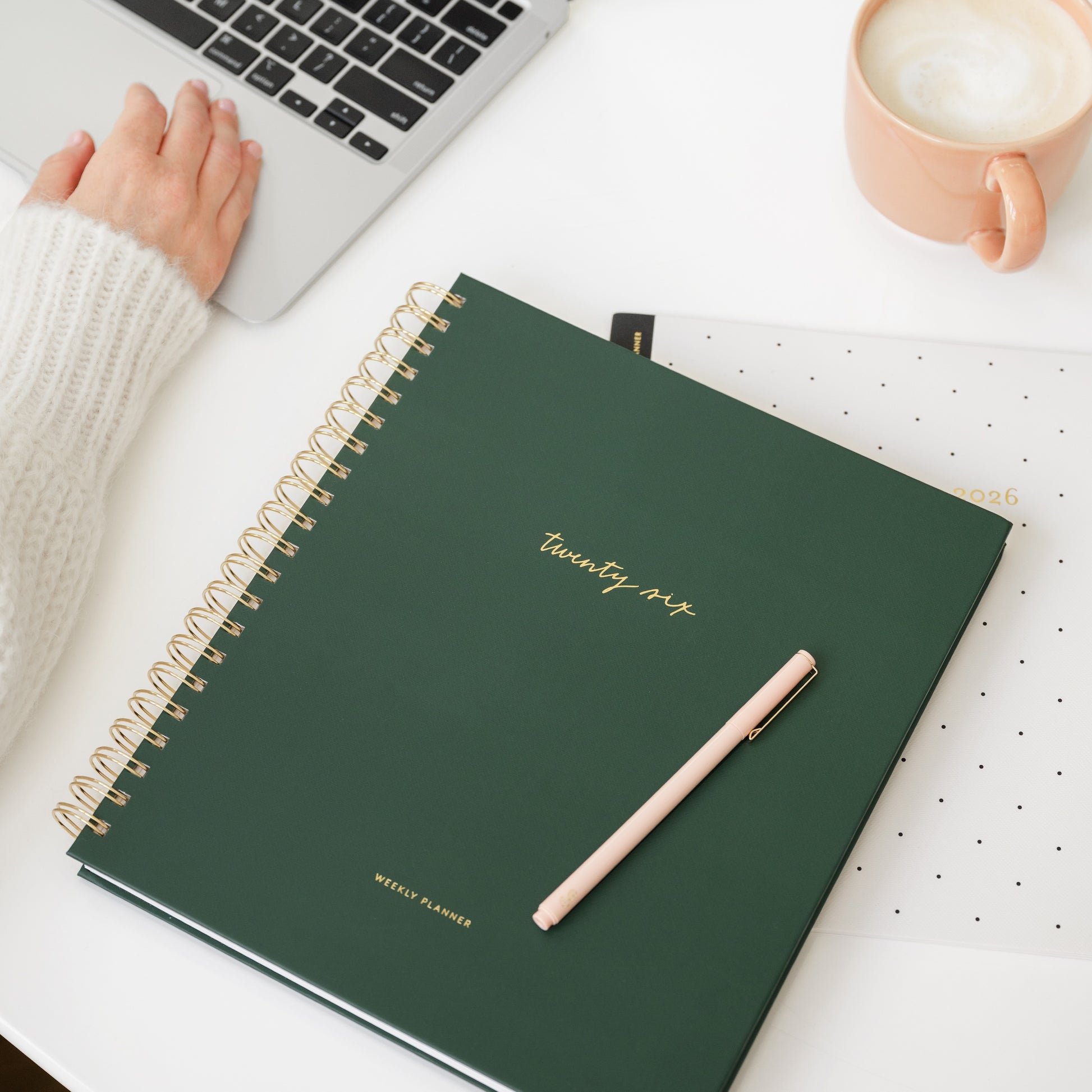 Green spiral planner with 'twenty six' on a desk with a laptop and mug