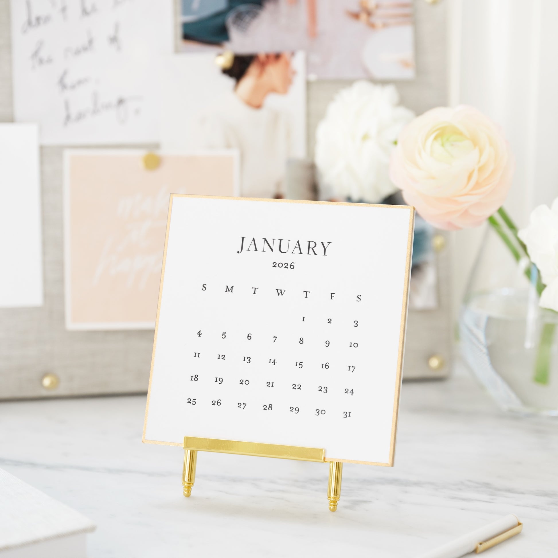 January 2026 calendar printed in black on white cardstock on brass stand with pretty inspirational board in background