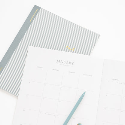 Blue stripe monthly 2026 planner with cover and open to monthly grid for january