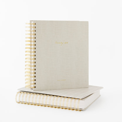 Two beige spiral planners with gold wire binding stackced