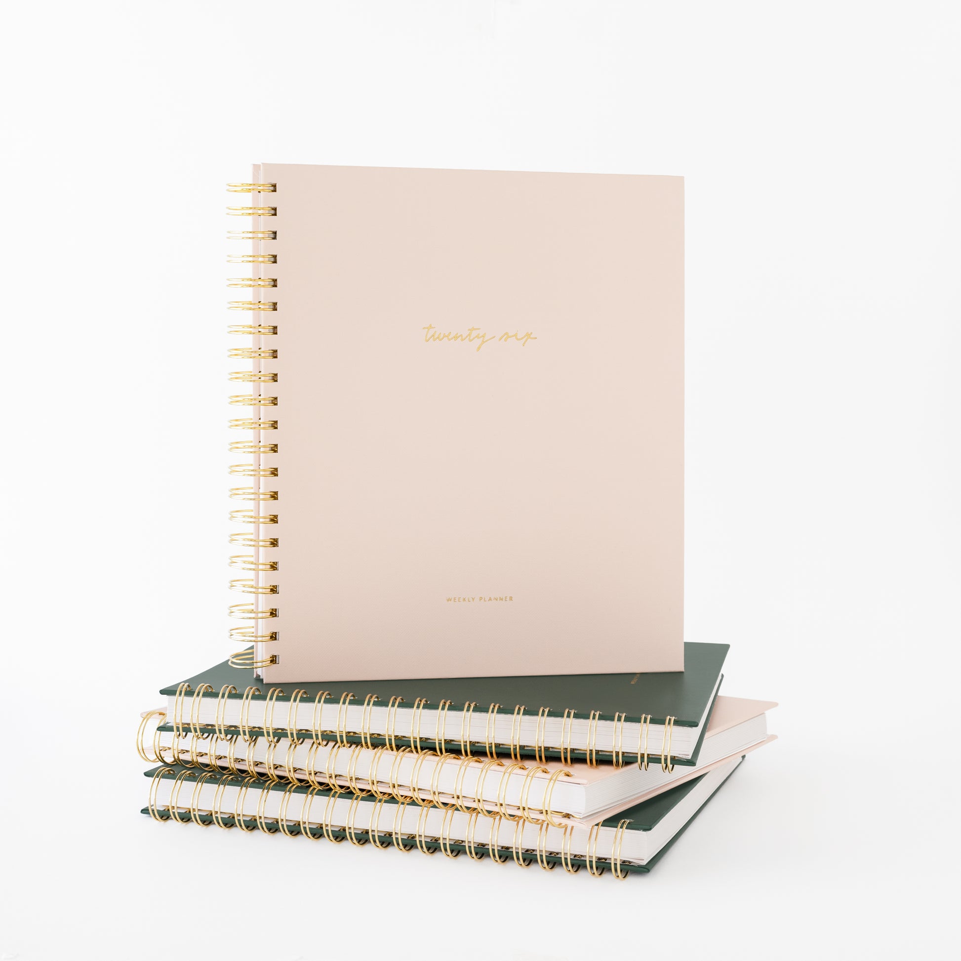 Blush spiral planner on top of stack of green and pink planners