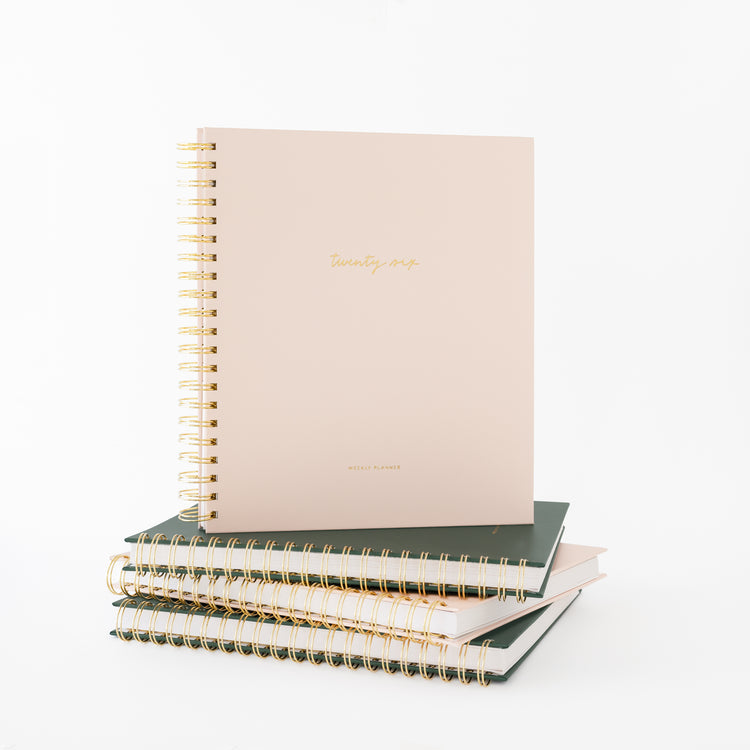 Blush spiral planner on top of stack of green and pink planners