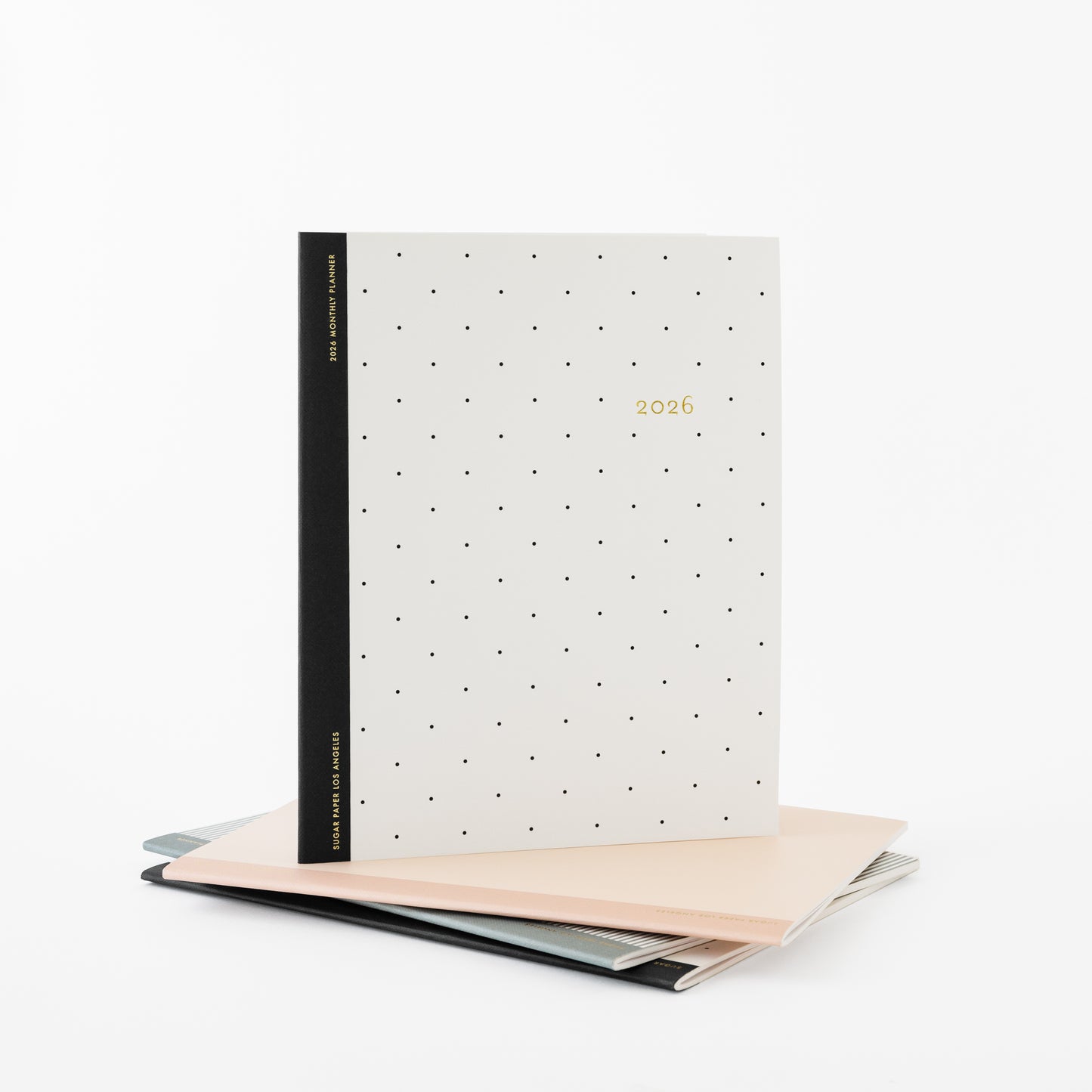 Monthly planner with polka dot design and black binding on stack of pink and blue planners