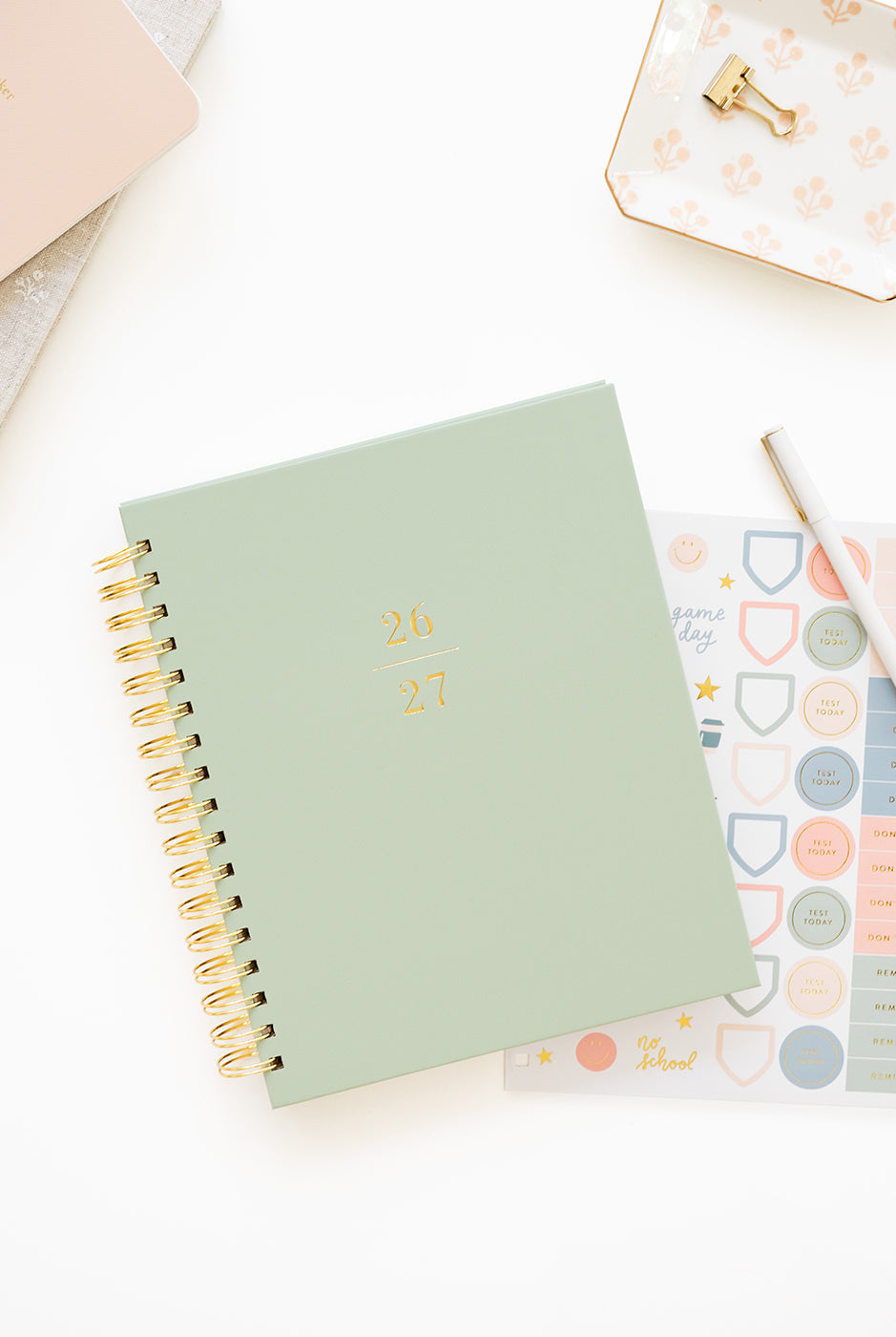 Light green spiral-bound planner on a white surface with decorative stickers and a pen.
