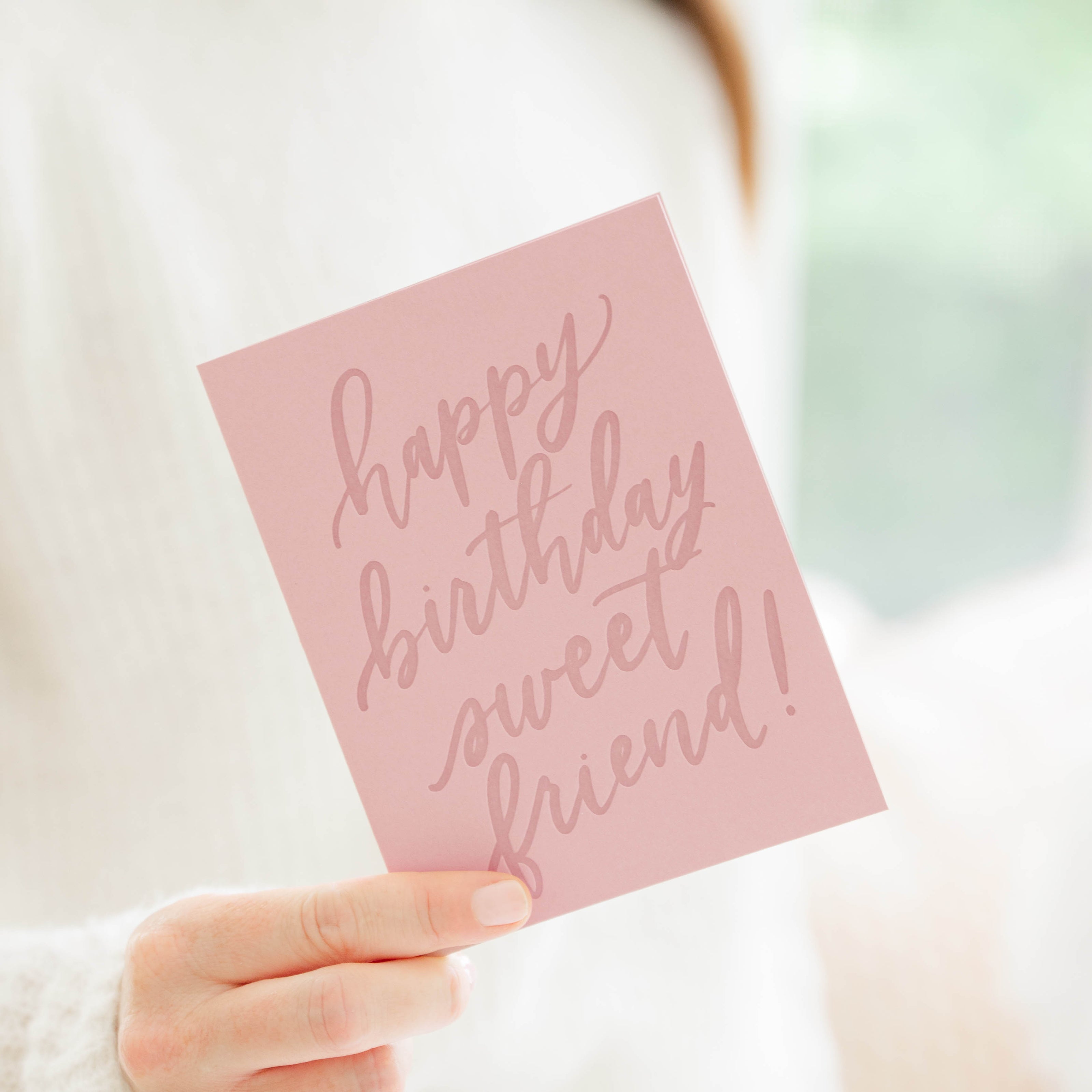 Hand holding a pink card with 'happy birthday sweet friend!' text