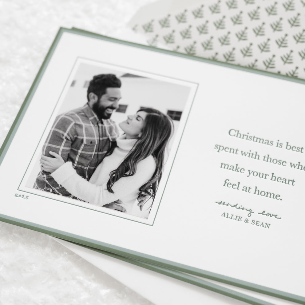 Custom holiday photo card with a photo of a couple and a Christmas message with green painted borders and a green tree liner