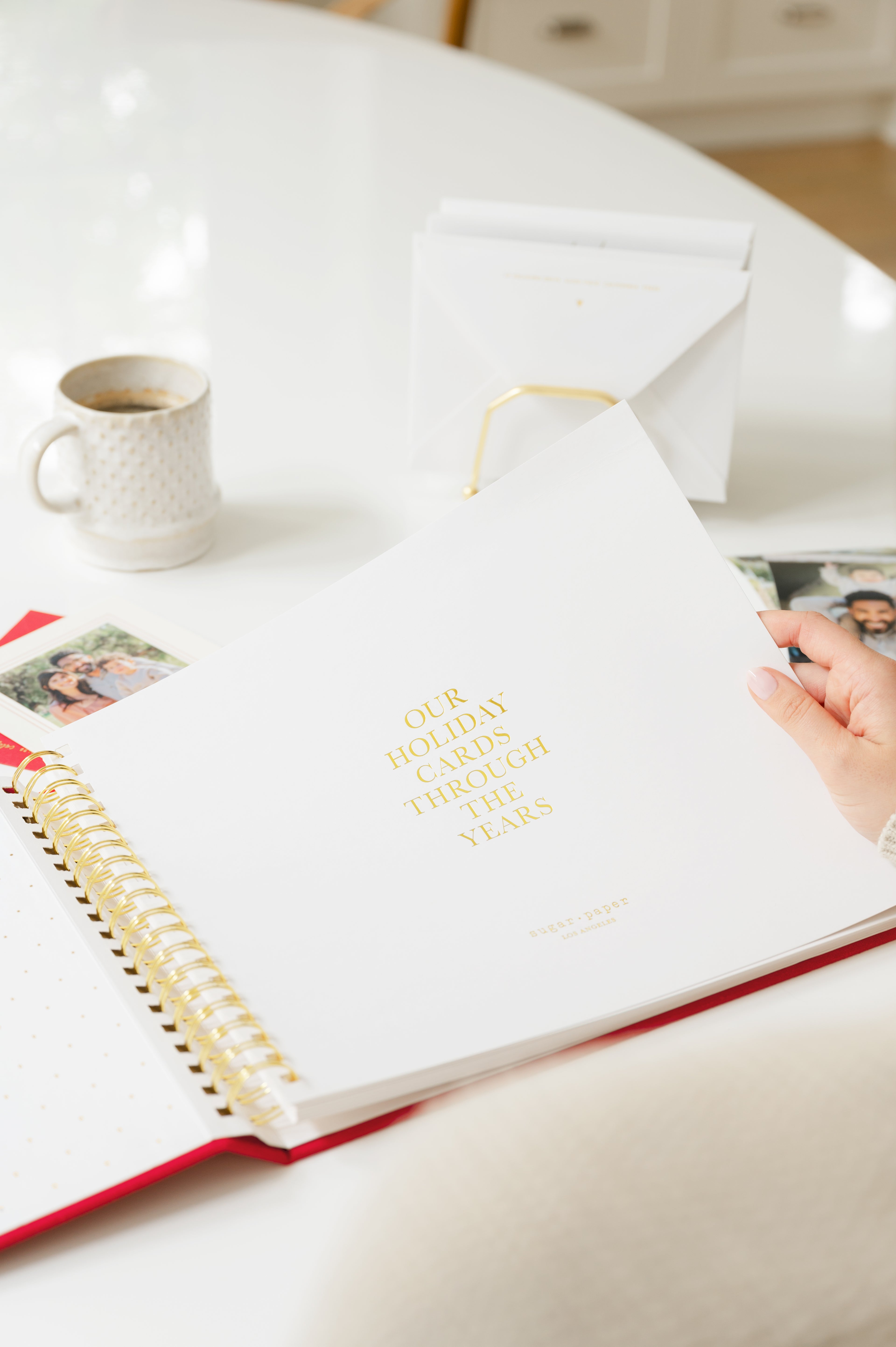 Person holding a red holiday card book open to our holiday cards through the years with extra photos and cup of coffee