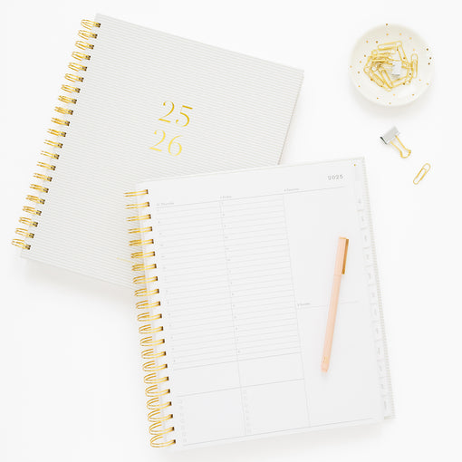 Flax and white striped spiral academic planner showing cover foil stamped with the dates 2025 and 2026 and the planner open to the weekly page with timed blocking for each day of the week