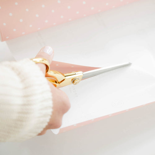 Woman cutting wrapping paper with gold scissors