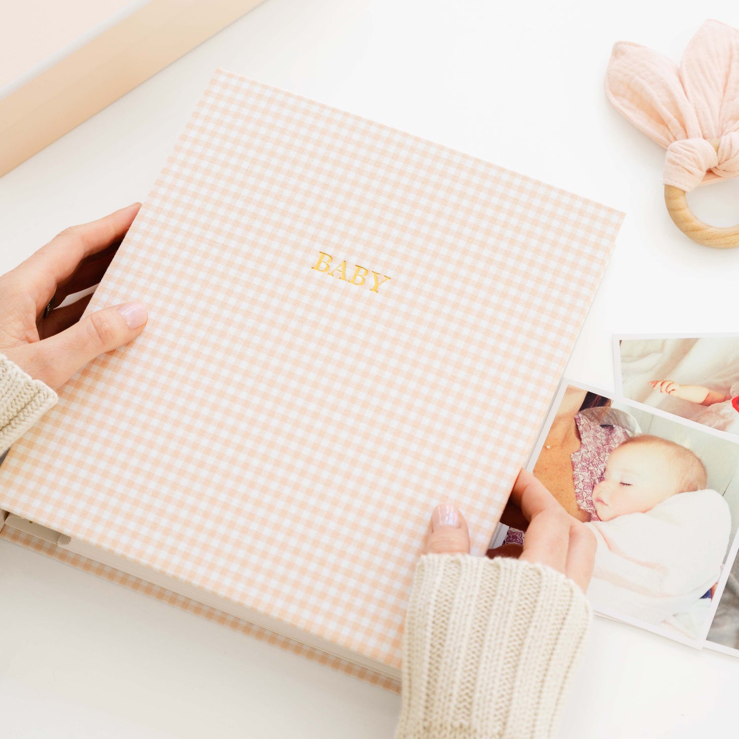 Person holding a baby photo album with 'BABY' on the cover, surrounded by baby photos and items.