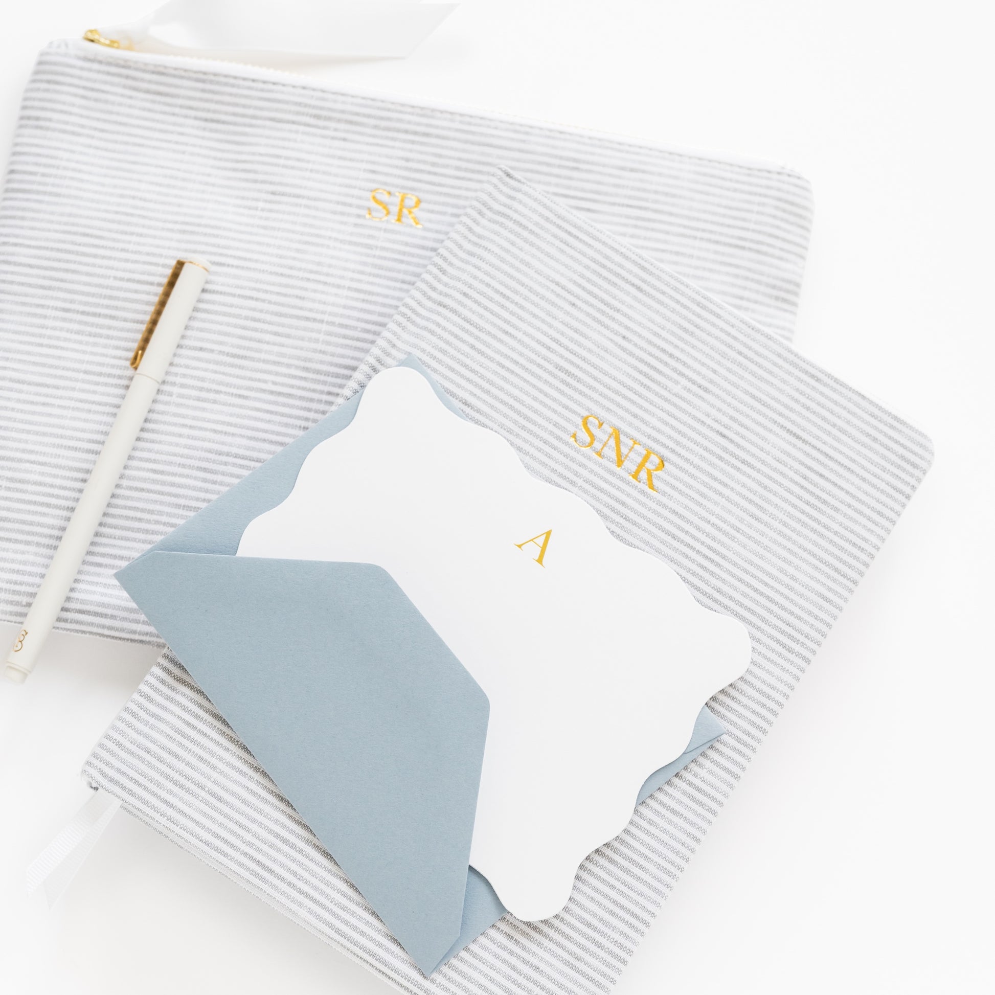 Grey striped fabric journal with 'SNR' initials and grey striped pouch with 'SR' initials with a white scalloped card and blue envelope with 'a' in gold foil