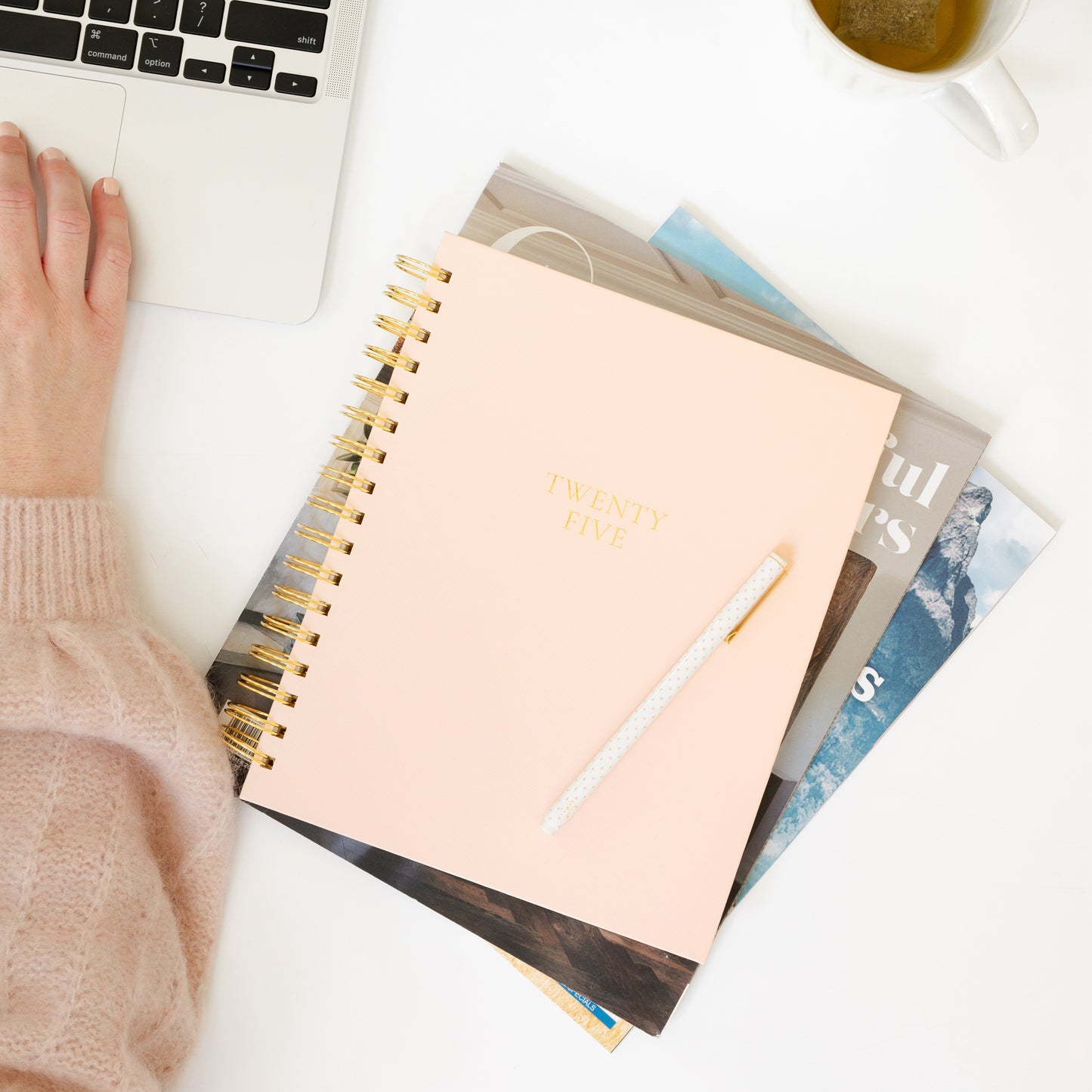 Pale pink spiral planner on desk with computer travel inspired