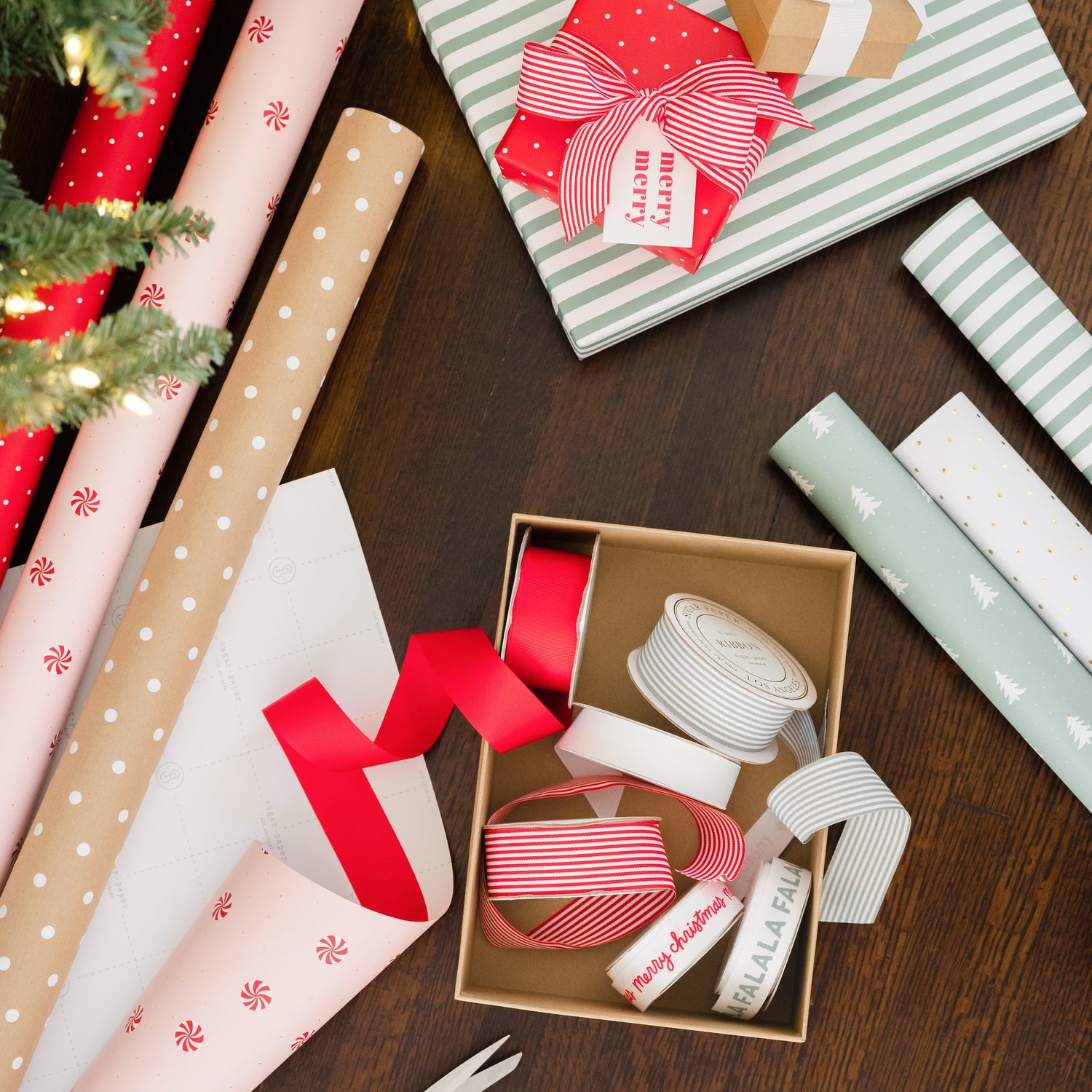 Gift wrap with ribbons, wrapped gifts, and wrap rolls on a wooden floor.