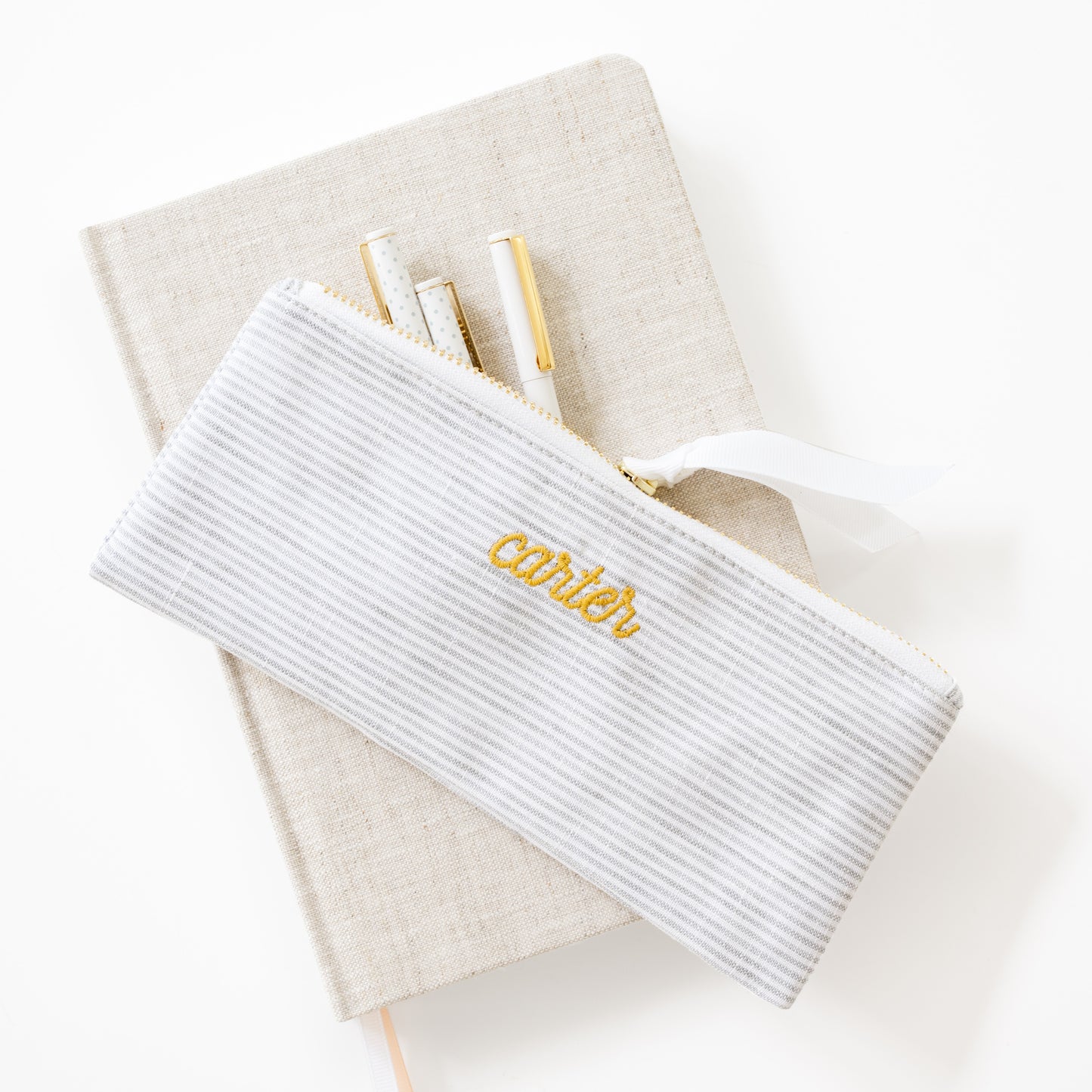 White stripe  pouch with 'carter' embroidery on a beige fabric journal with pens inside
